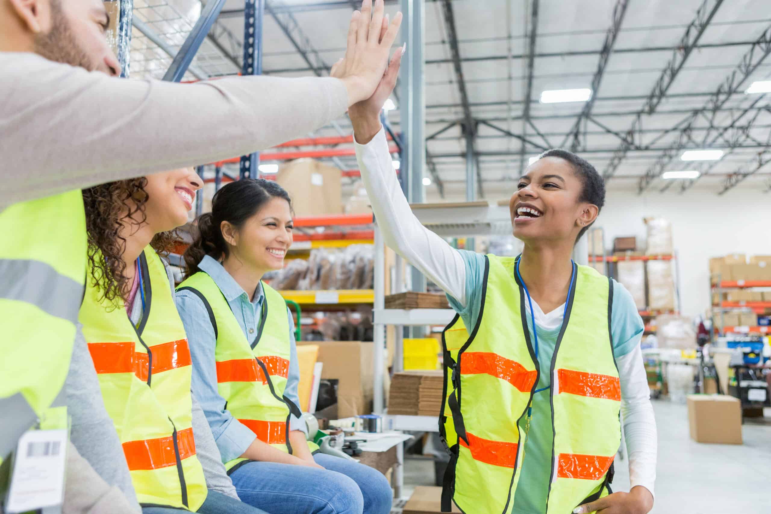 A joyful moment captured between two team members in high-visibility vests on the manufacturing floor, as they review data on a tablet, reflecting the positive team dynamics and quality-centric culture vital for industrial excellence.