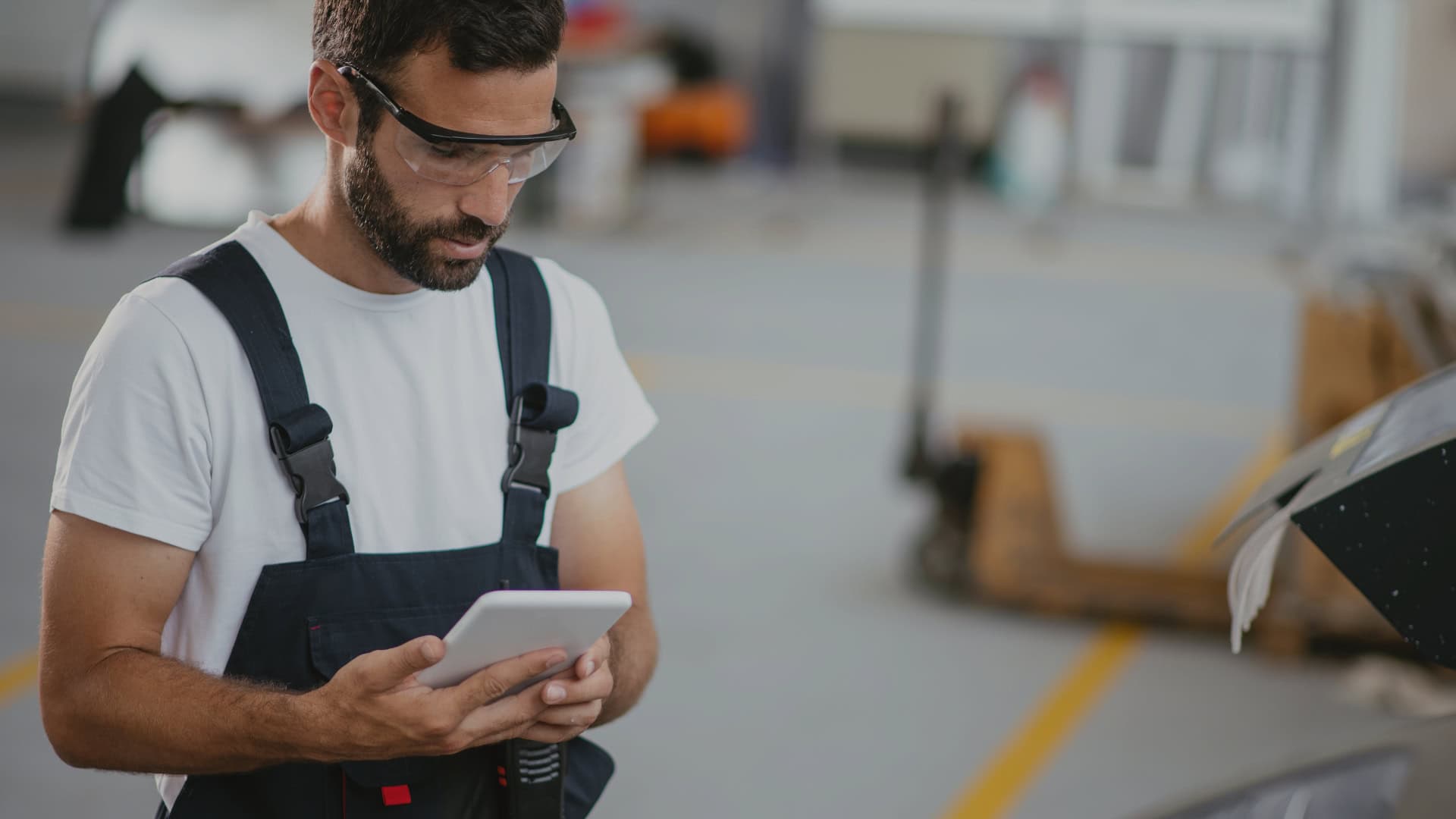 A factory worker in overalls reviewing digital work instructions on a tablet, ensuring accuracy and efficiency in the production process.