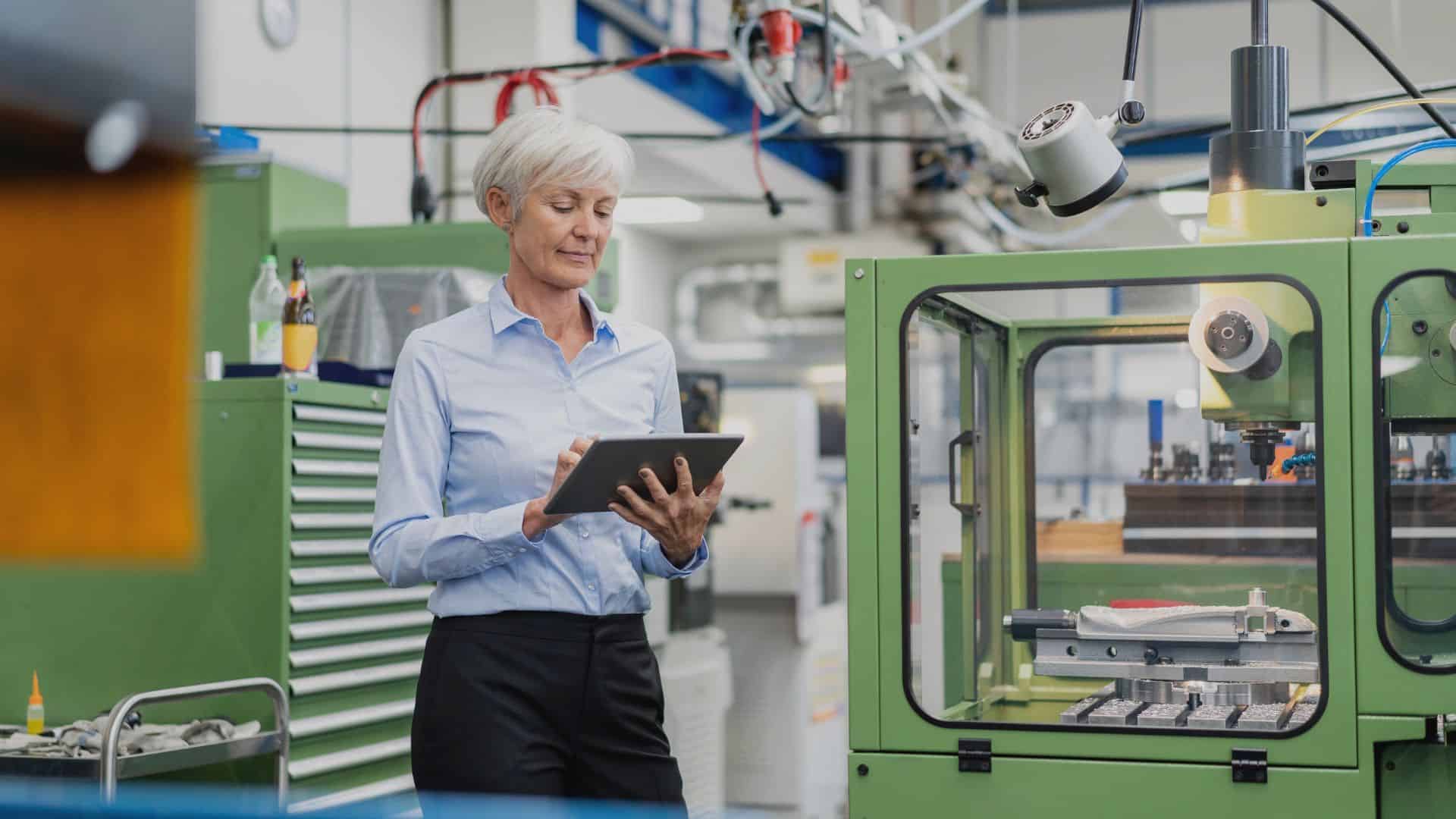 A senior manufacturing manager using a tablet to monitor traceability processes in a modern production facility.